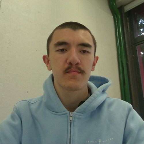 Person with a mustache, wearing a light blue hoodie, in front of the edge of a window.