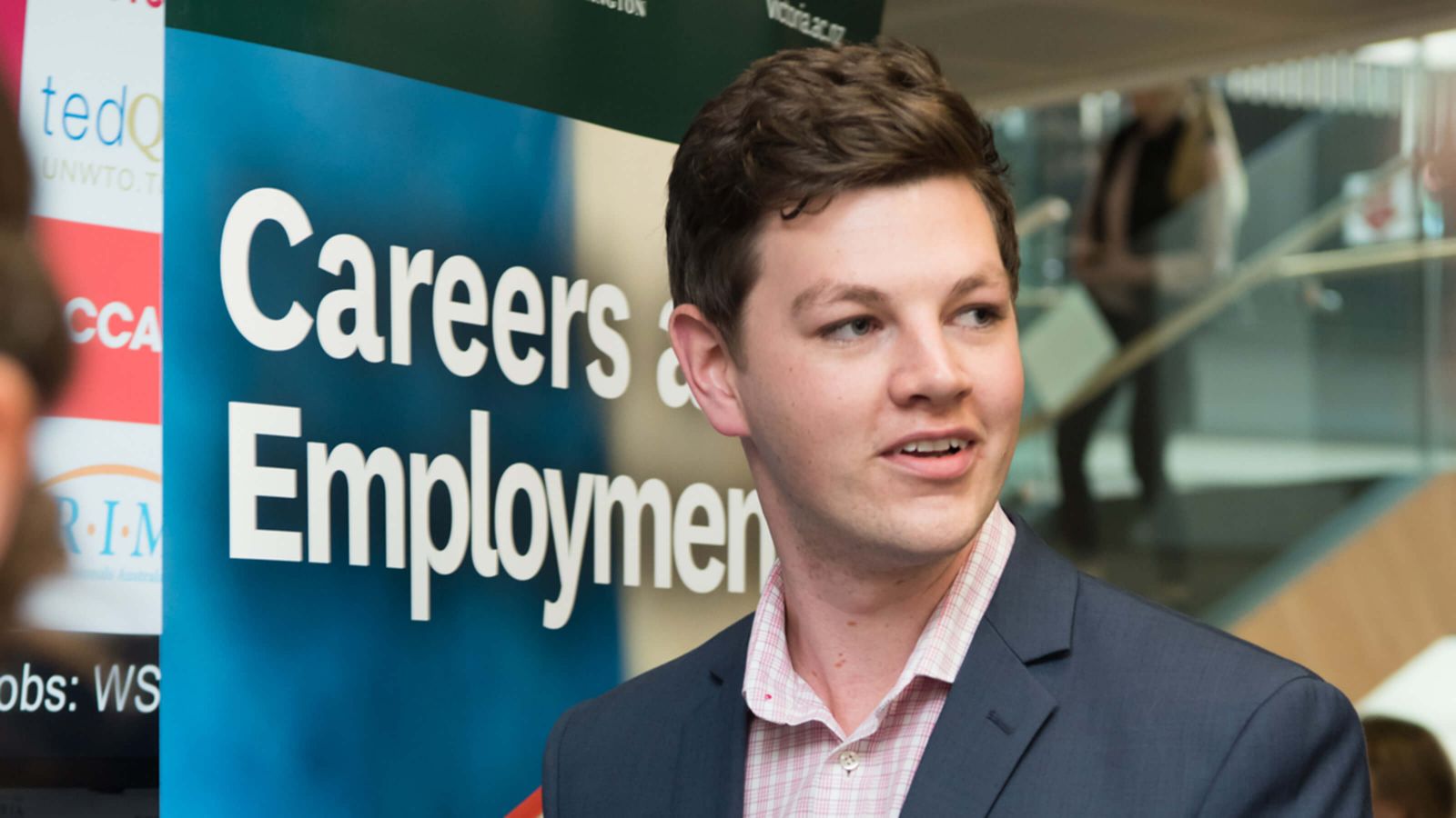 A young male Pakeha business student wearing a suit jacket and pink shirt at a Careers expo