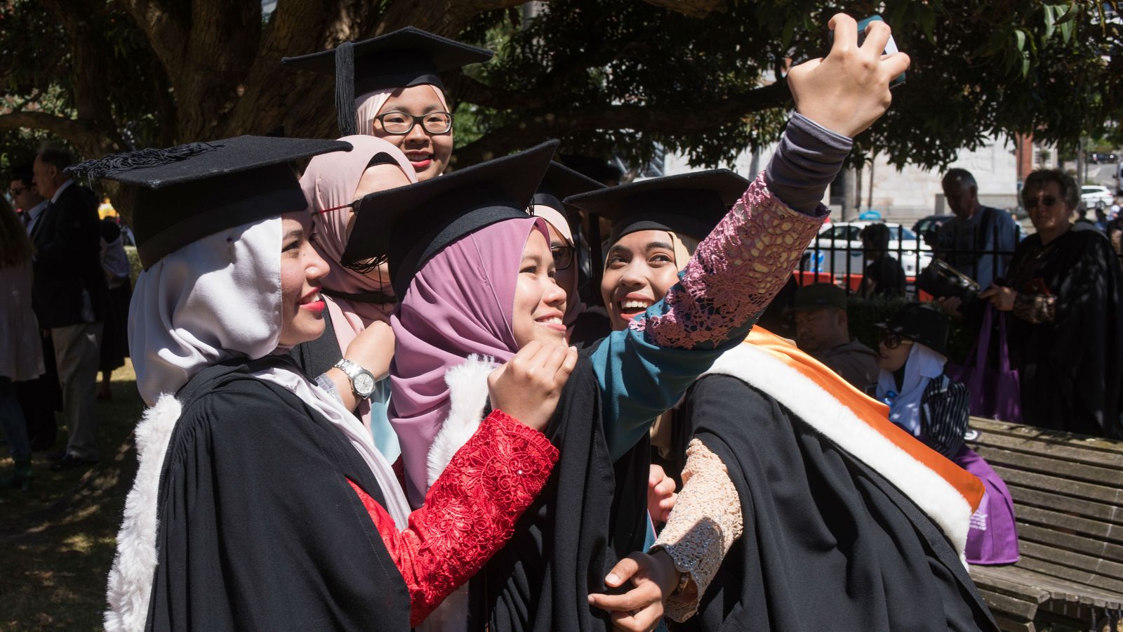 A group of international students dress in their graduation robes, smile together for a selfie.