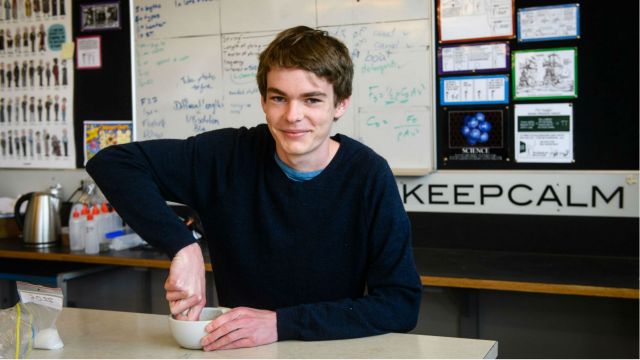 Finn Messerli, sits at a table with his hands around a bowel, behind him is a white board and a sign saying 'keep calm’.
