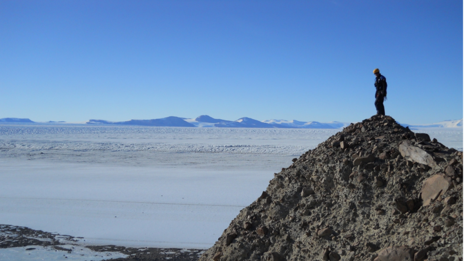 Tim stands on a rocky hill overlooking Antarctic ice