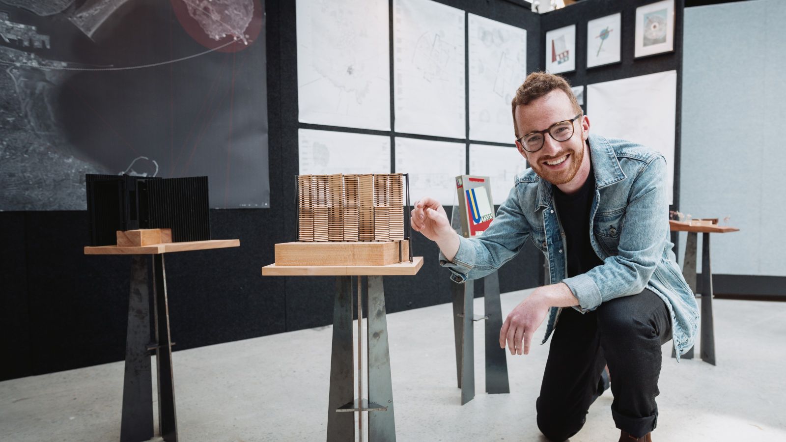 patrick kelly crouches with wooden architectural model in exhibition of architectural models and maps