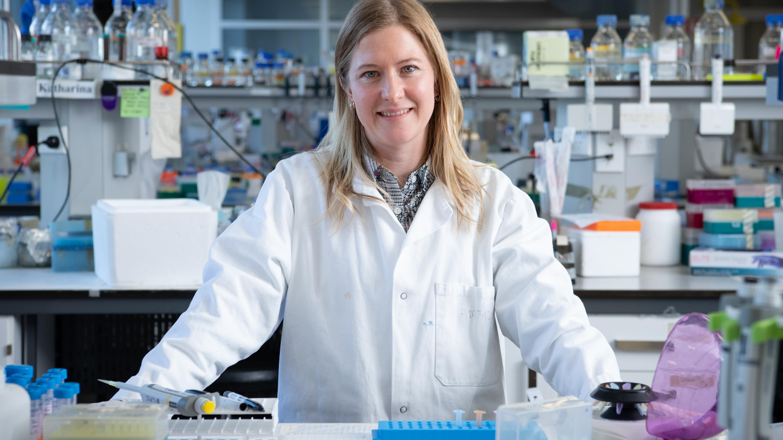 Girl with blonde hair in lab coat amongst scientific gear including phials, pippettes, test tubes