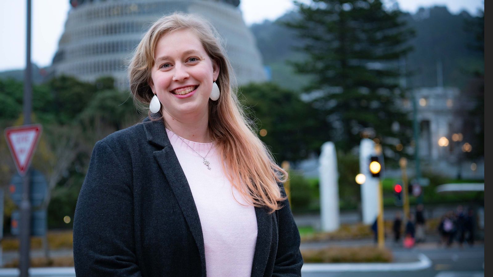 A woman in professional attire stands outside by parliament in Wellington.