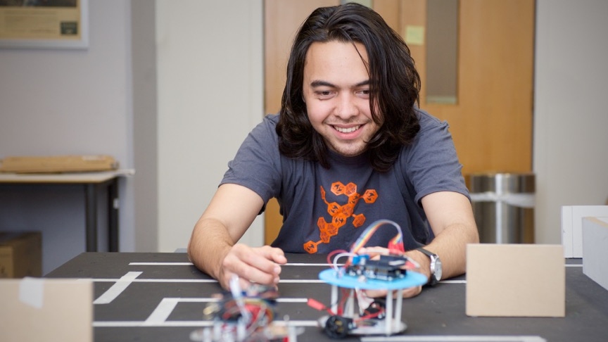 Grayson Hughes looks at a robot navigating a table. 