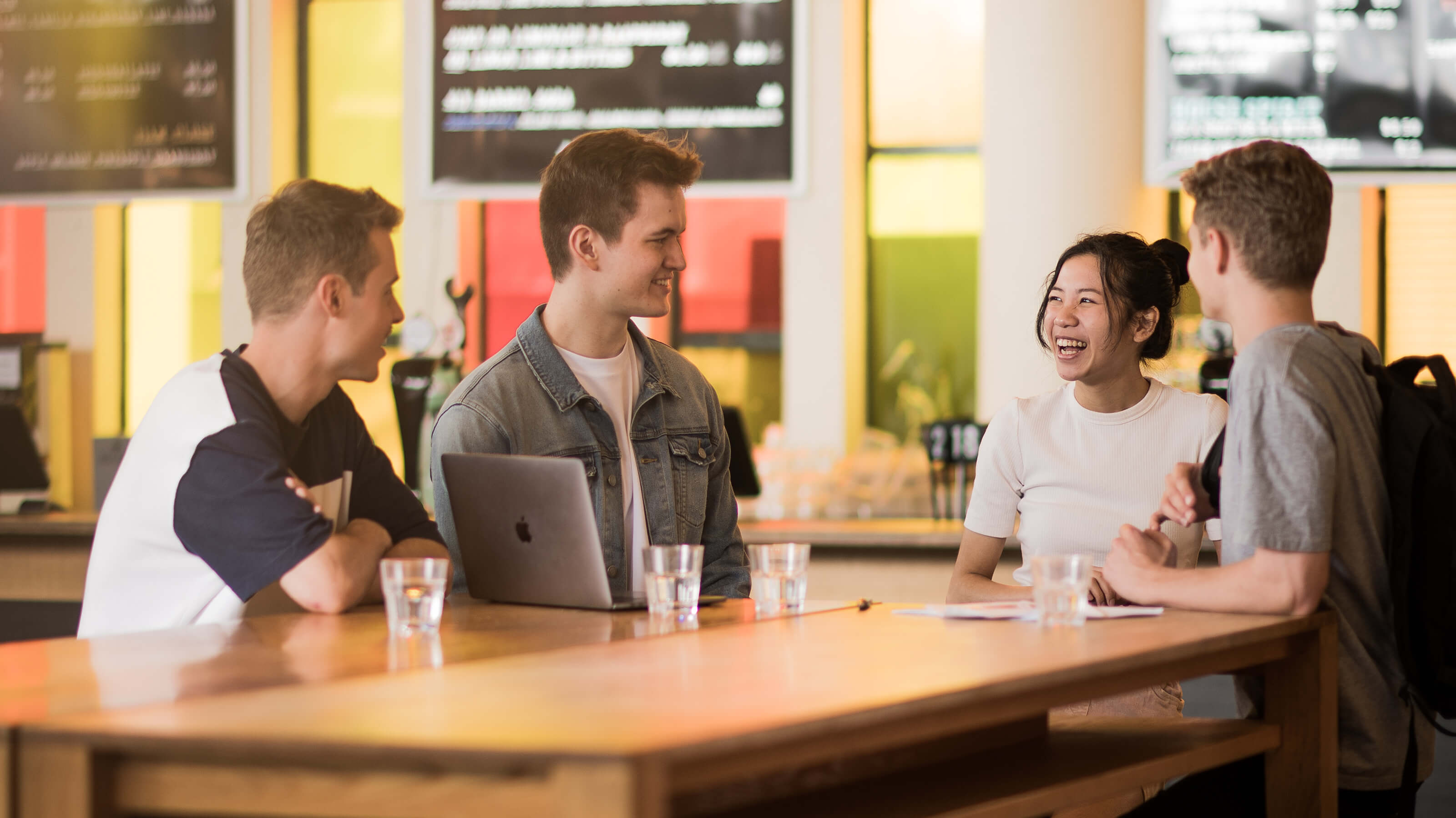 Four students gathered around a table and laptop having a chat.