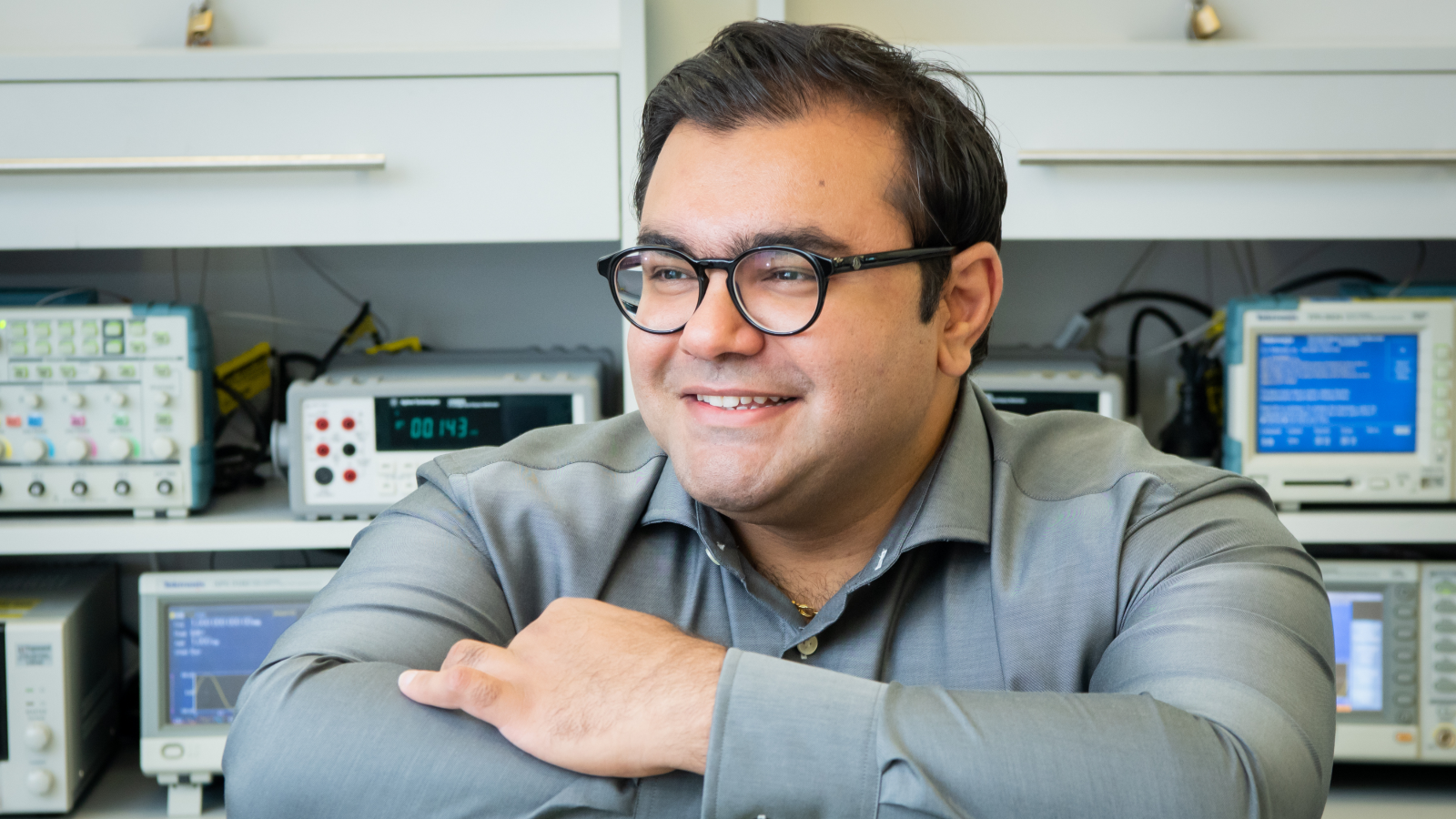 Smiling man with short dark hair in front of communications equipment. 