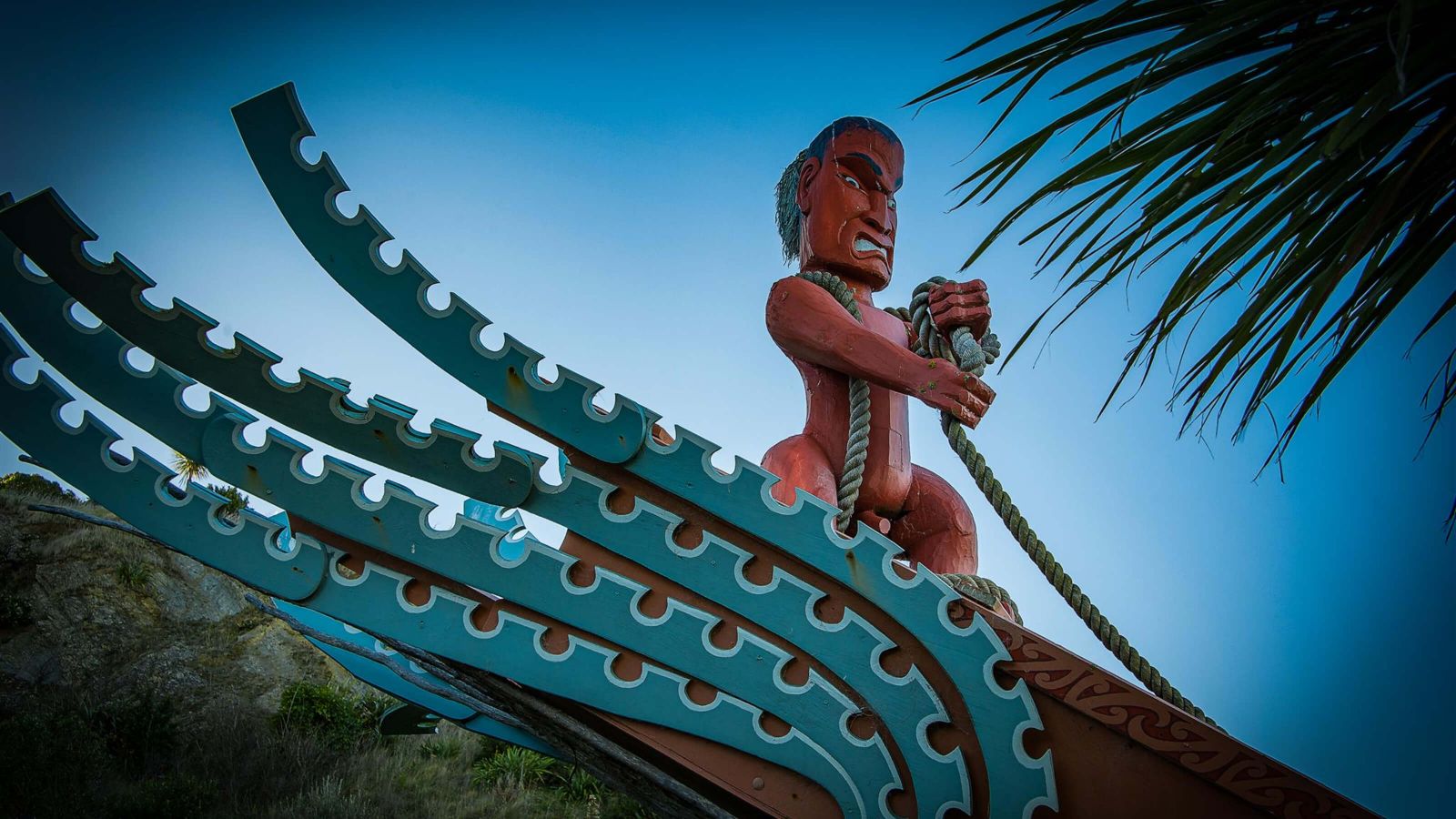 Close up of a Māori waka (canoe) with a warrior sculpture pulling on a rope.