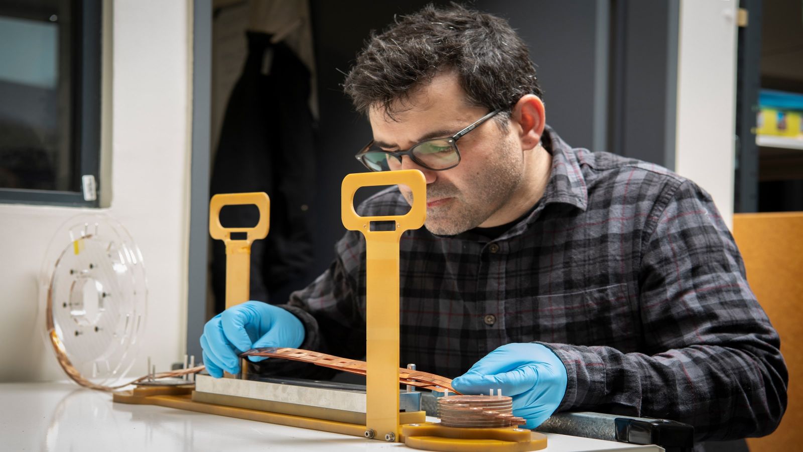 Scientist working at a desk holding superconductor tape in gloved hands