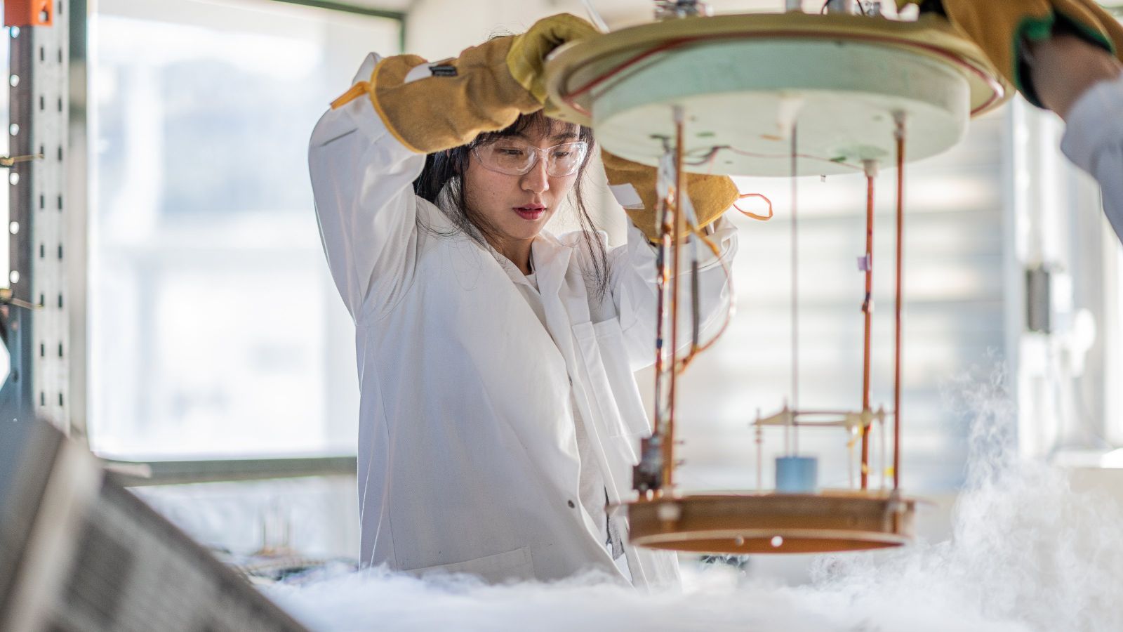 Female scientist lowering equipment into a vat of liquid nitrogen.