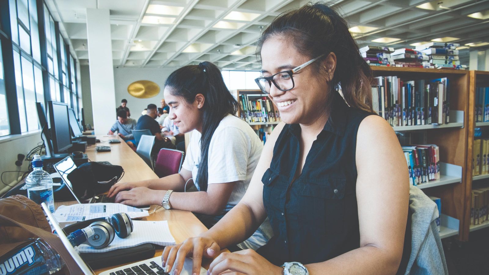Two female Pasifika students working on laptops in the library. 