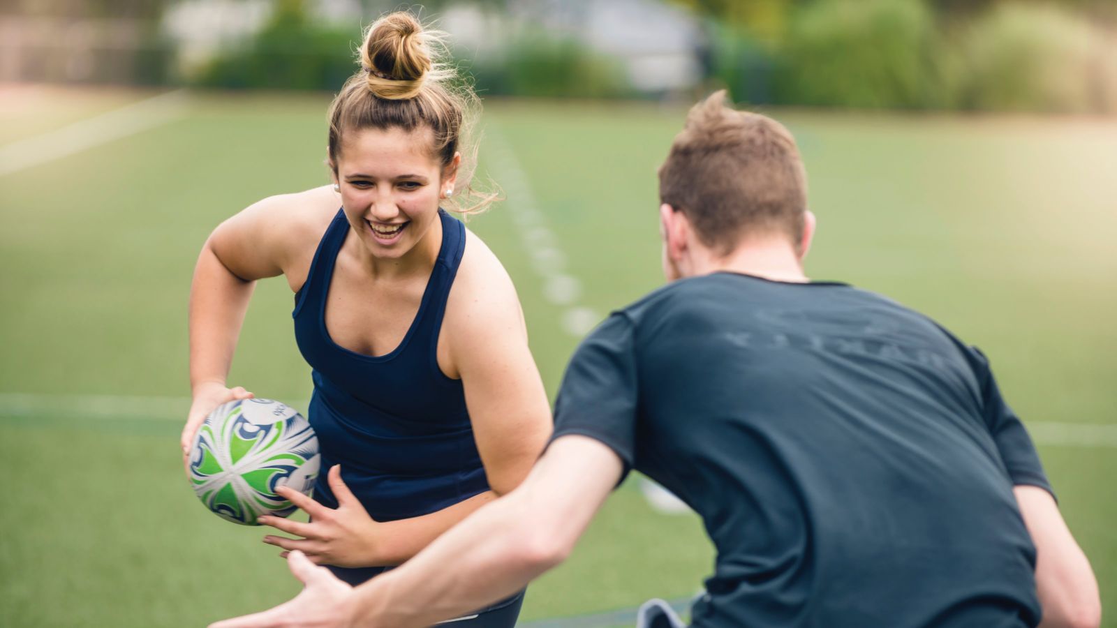 A young woman running with a rugby ball and trying to get around another player.