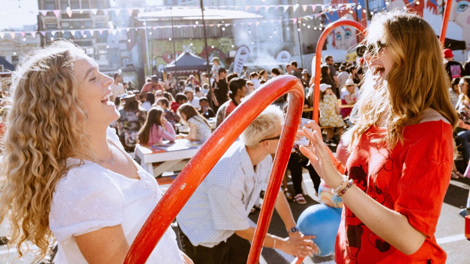 Two students at a sunny street party, holding balloons and laughing 