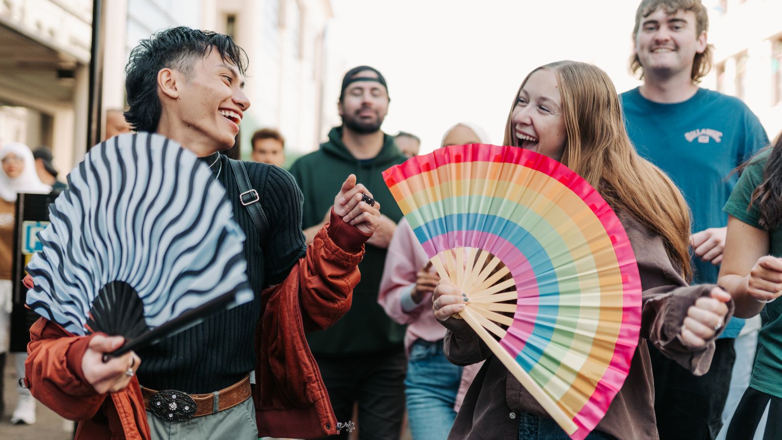 Two students in the street with a colourful rainbow fan