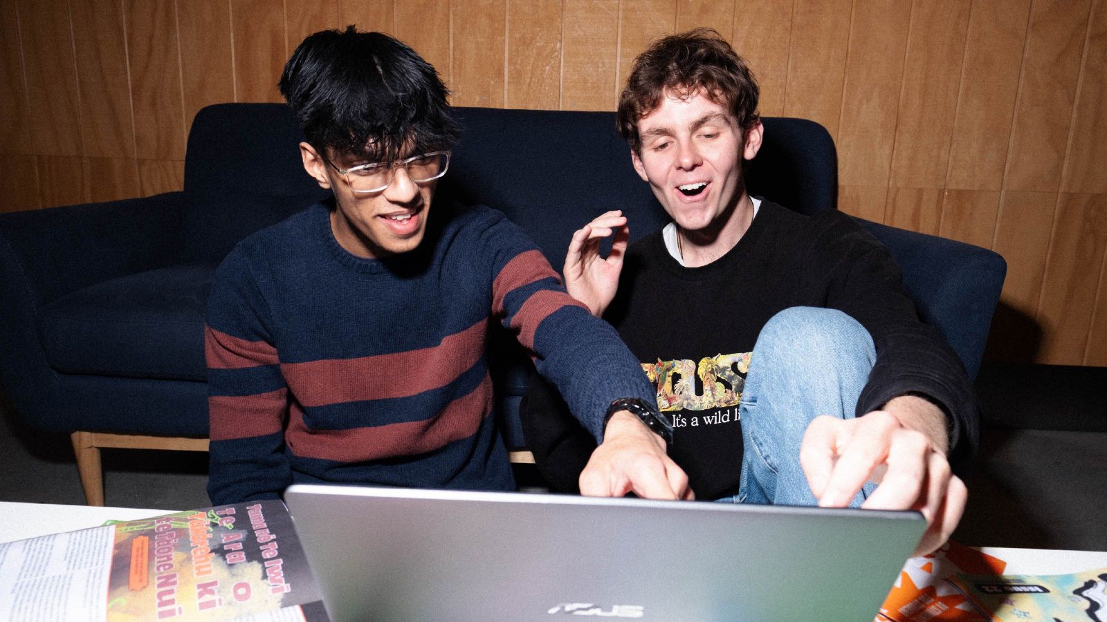 Two students looking at a laptop and laughing
