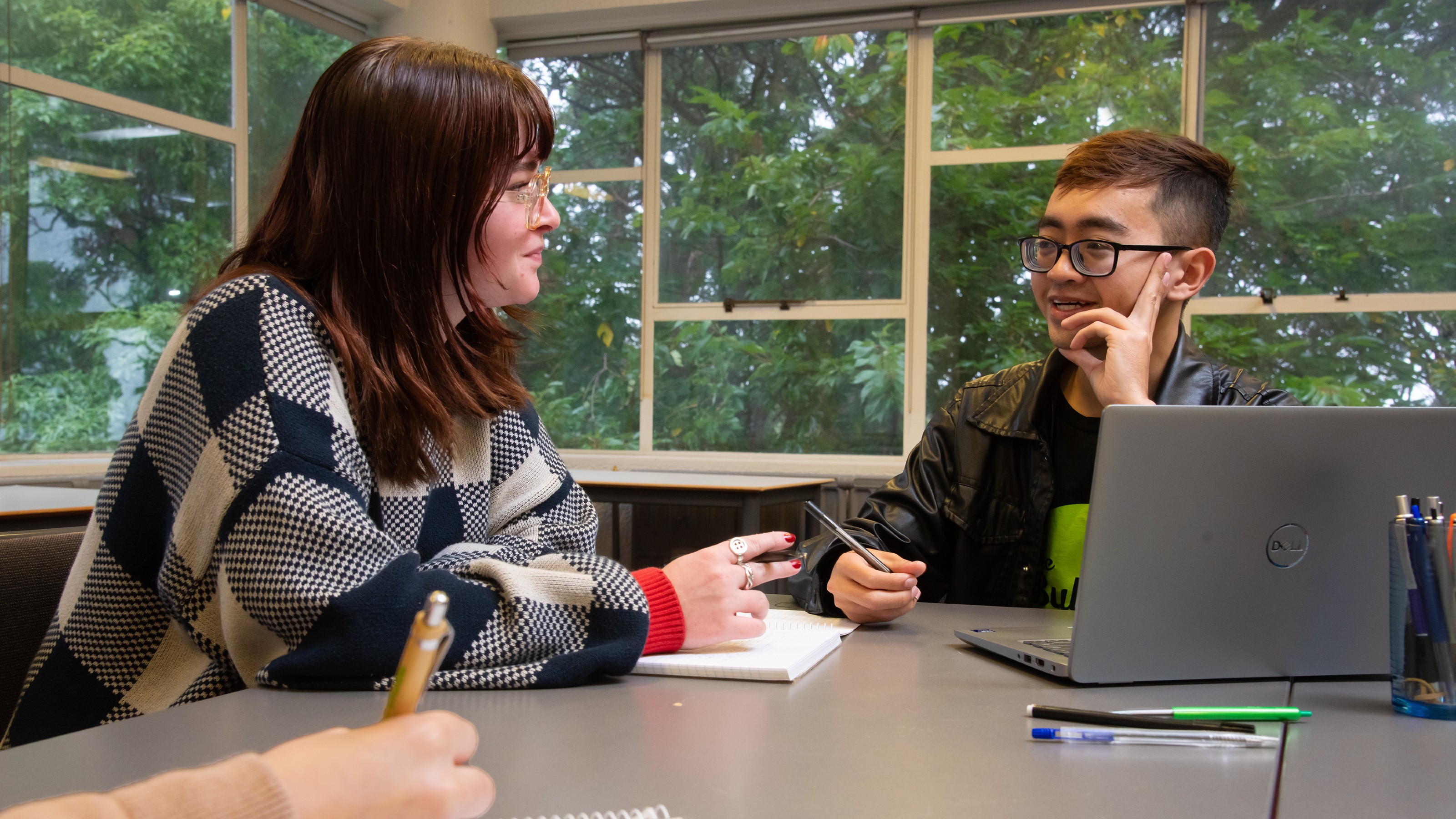 Two students in discussion as they write at a table in The Bubble at Kelburn with a notepad, pen, and laptop.