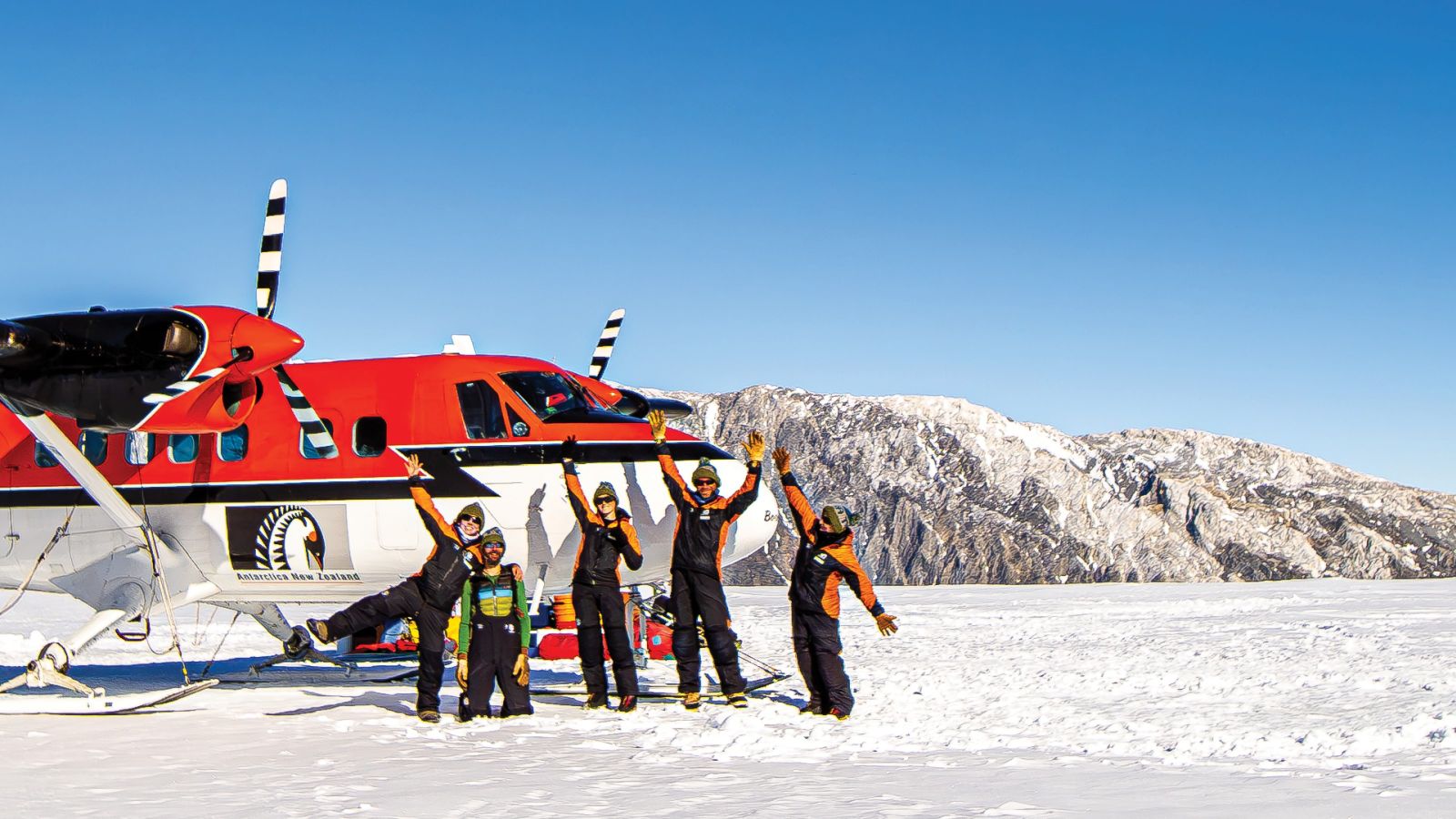 ARC students standing in the snow in Antarctica in front of a twin otter plane in the Antarctic with Mt Tuatara in the background and a bright blue sky
