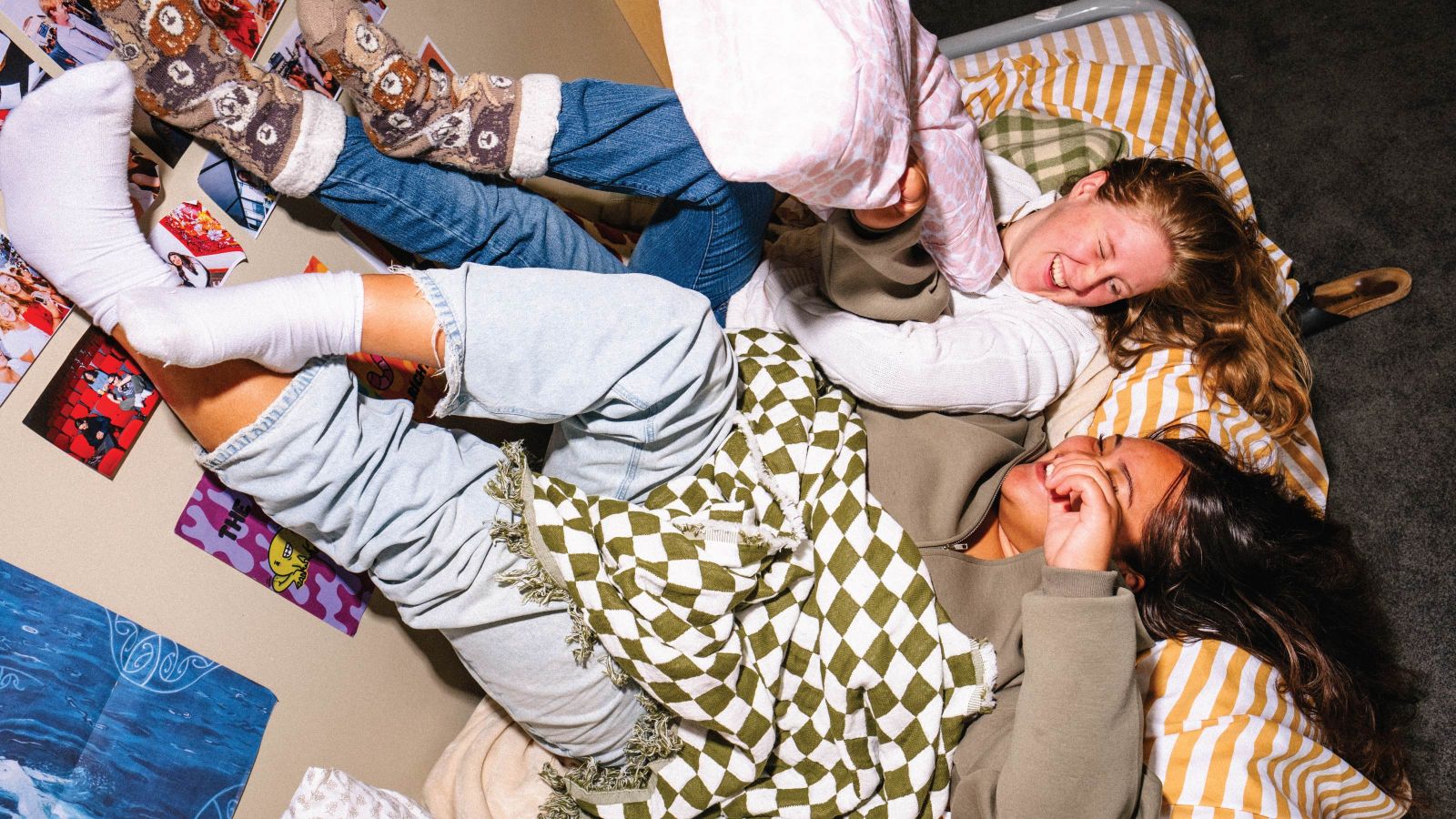 2 students relaxing on a bed in halls and laughing together. Their backs are on the bed and their feet are resting up against a wall.
