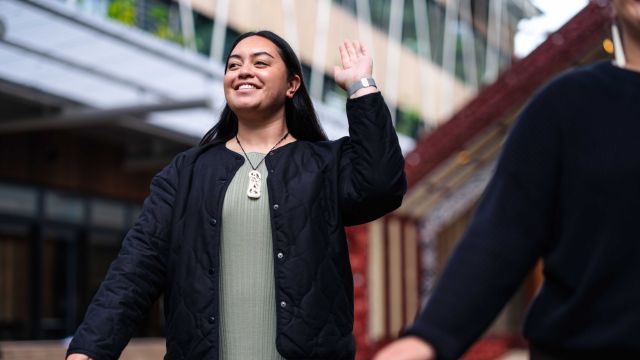 Young Māori woman making greeting gesture in front of the marae.