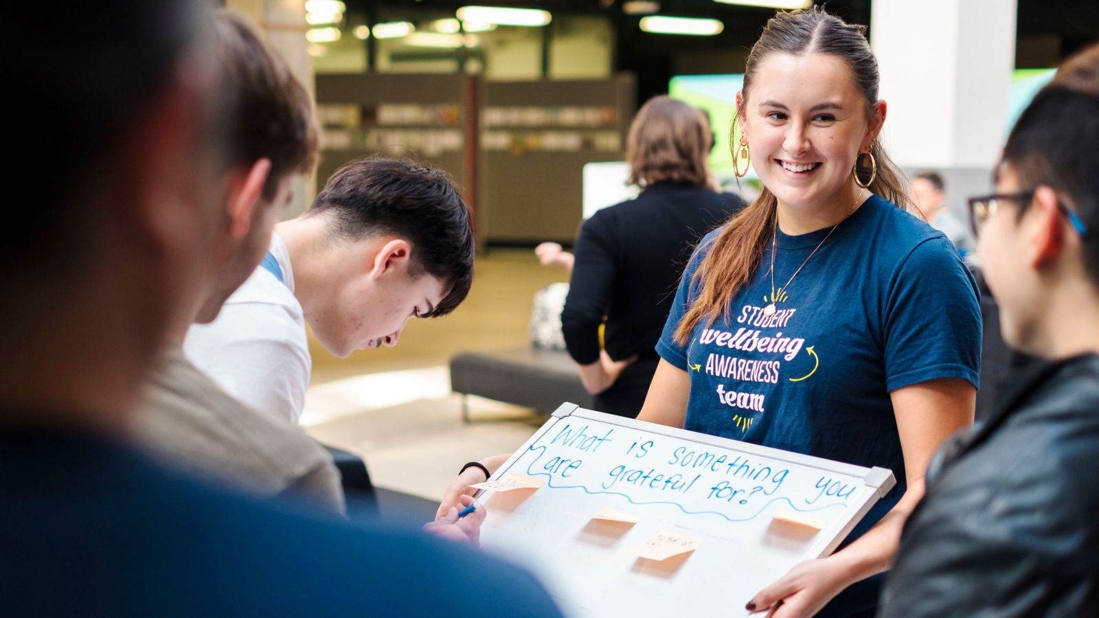 A Student Wellbeing Facilitator standing with the wellbeing board that says 