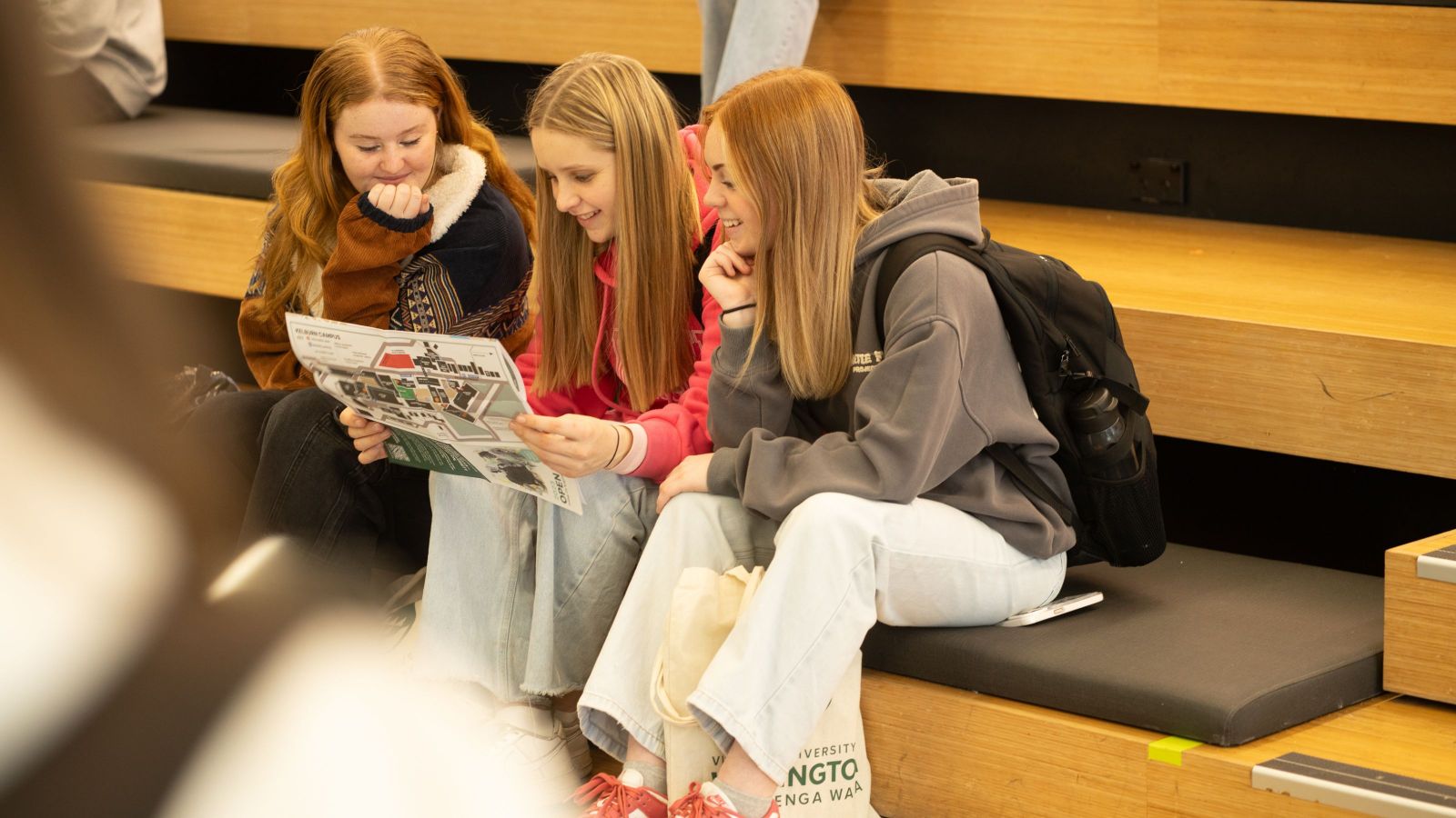 Three students sitting on indoor steps, looking at a campus map together.