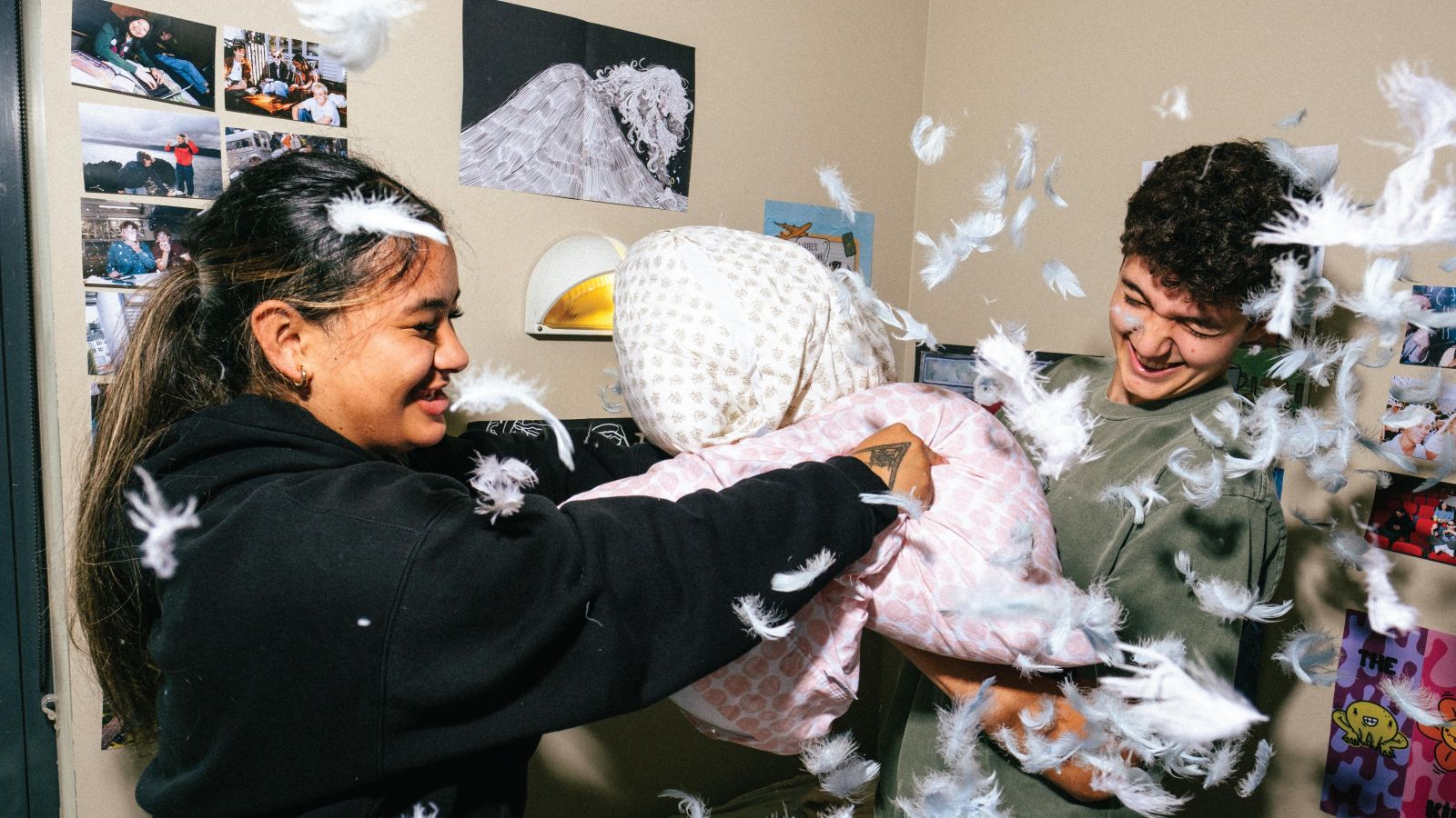 Two students pillow fighting in student accommodation, with feathers flying around.