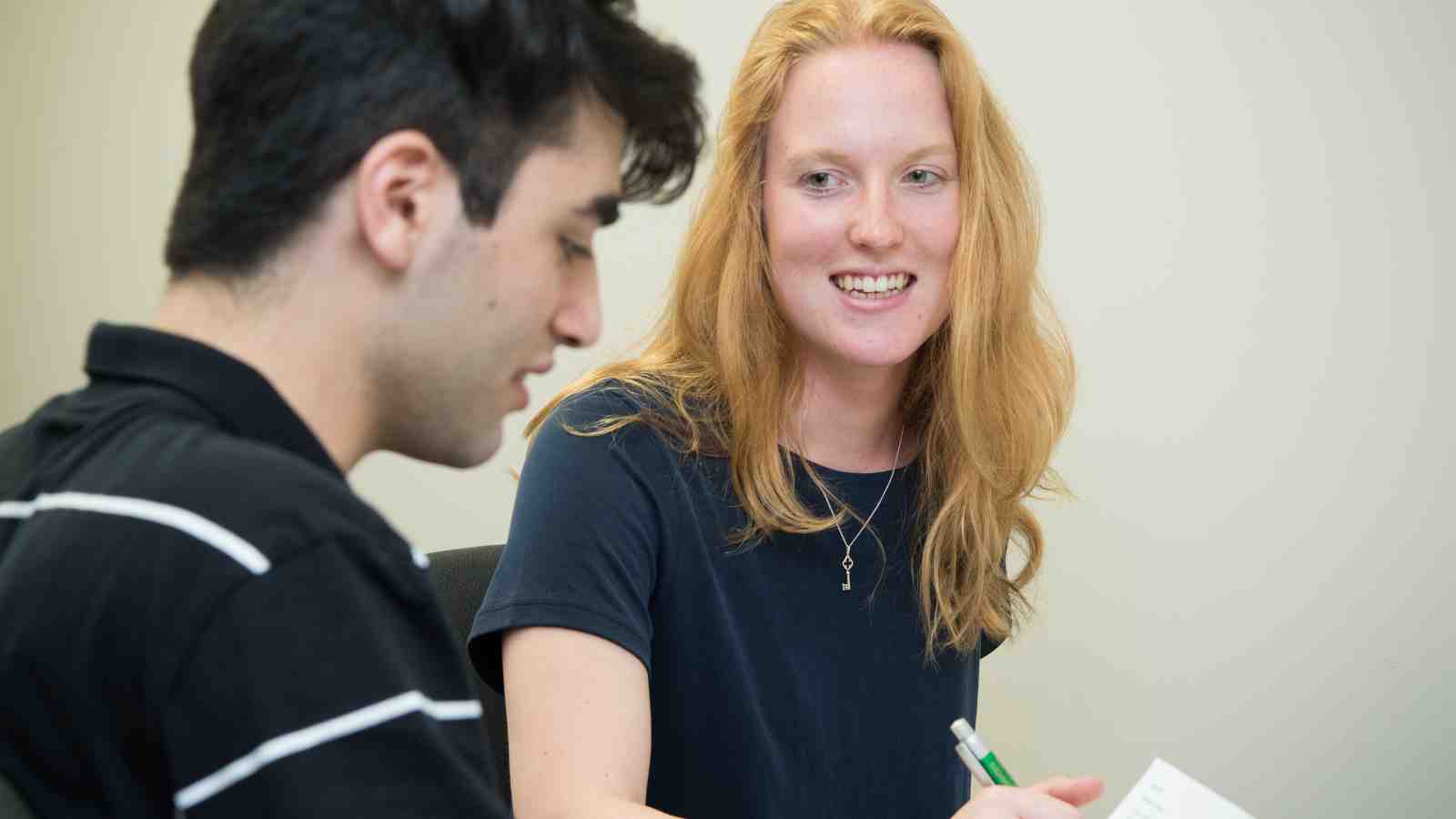 Lucy Woods, a young woman with long red hair, writing notes for a young male university student.