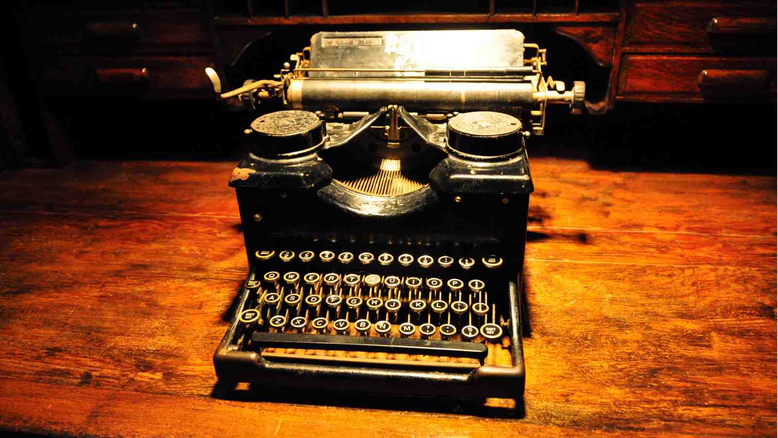 An image of an old black typewriter on a wooden desk.