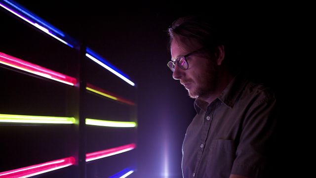 Nicolas Bernier in a dark room looking a tubes of light – photo credit: Caroline Campeau.