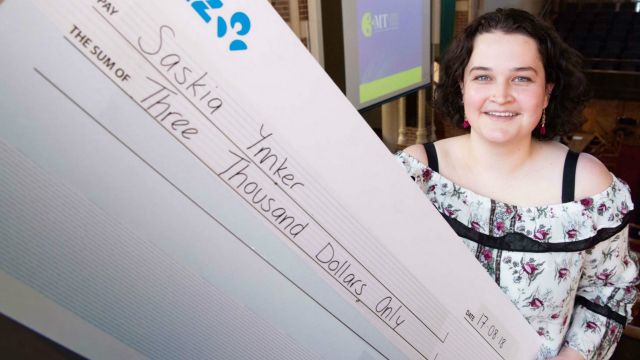 Saskia Ymker holds a large cheque of three thousand dollars for winning a 3MT competition.