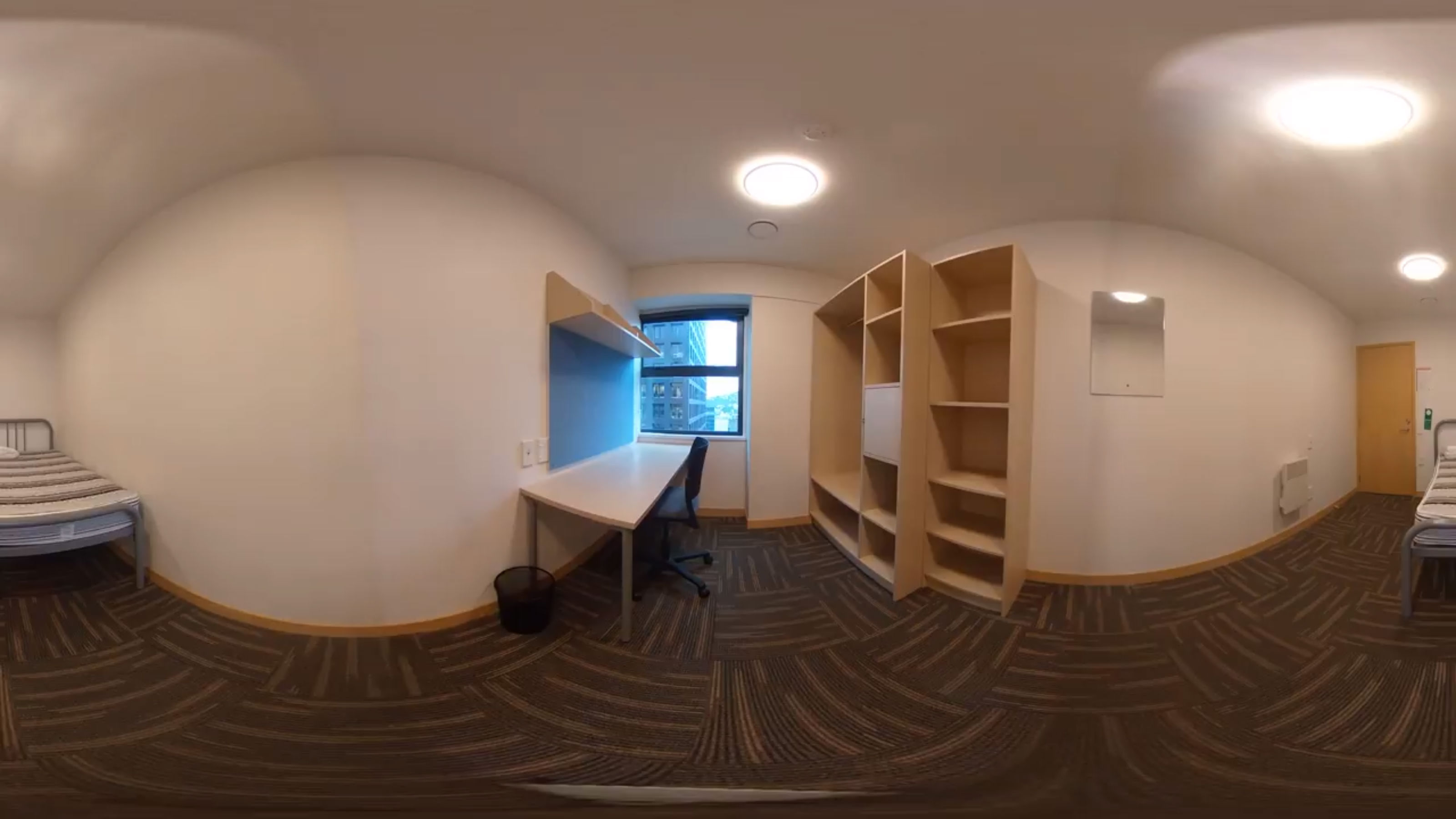A panoramic view of a single room with a desk and empty wardrobe.