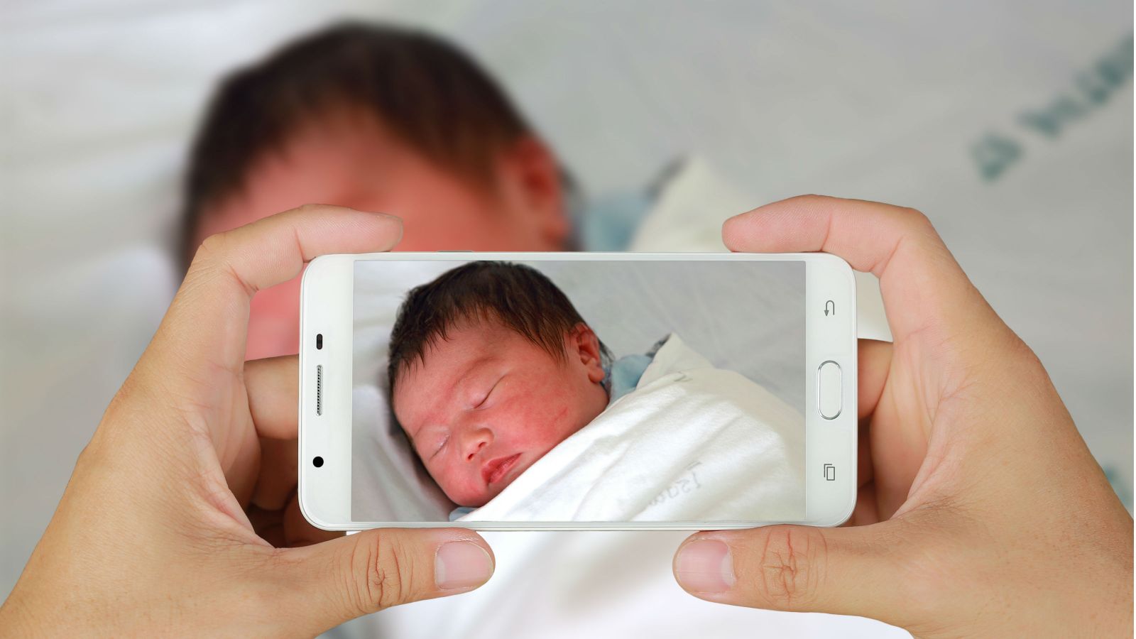 A new born baby being captured on by the camera of a smartphone.