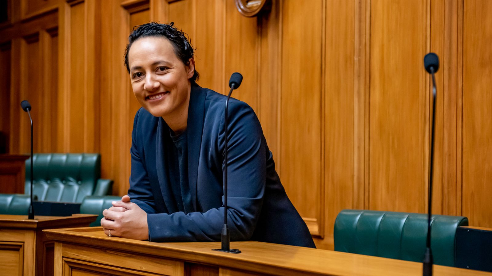 MP Kiritapu Allan leans forward from a green leather chair onto a rimu timber bench in the grandly furnished heart of New Zealand Parliament, the Chamber.