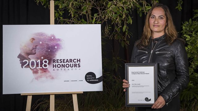 Arini with her award standing beside a poster that reads, “2018 Research honours Aotearoa”.