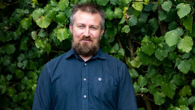 A profile image of Jonathan West by green bushes.