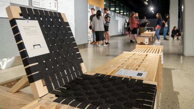 wooden bench with backrest and woven black fabric seat at front of exhibition of wooden furniture