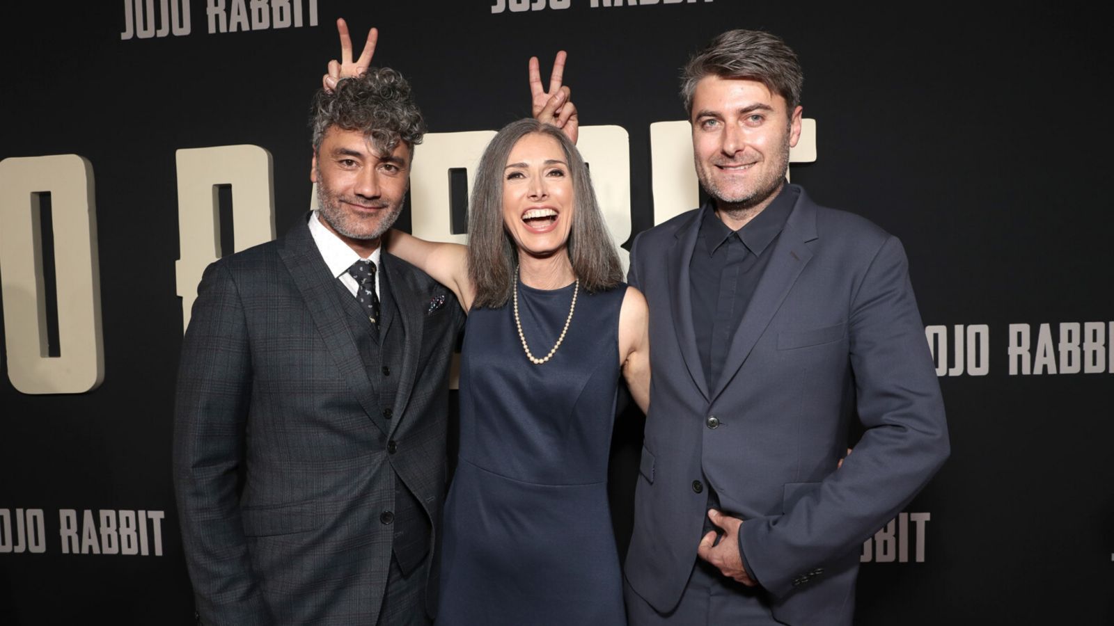 Taika Waititi, Christine Leunens and Carthew Neal at the premiere of Jojo Rabbit (Fox Searchlight) – Taika and Christine hold their fingers over eachothers head in the form of rabbit ears.