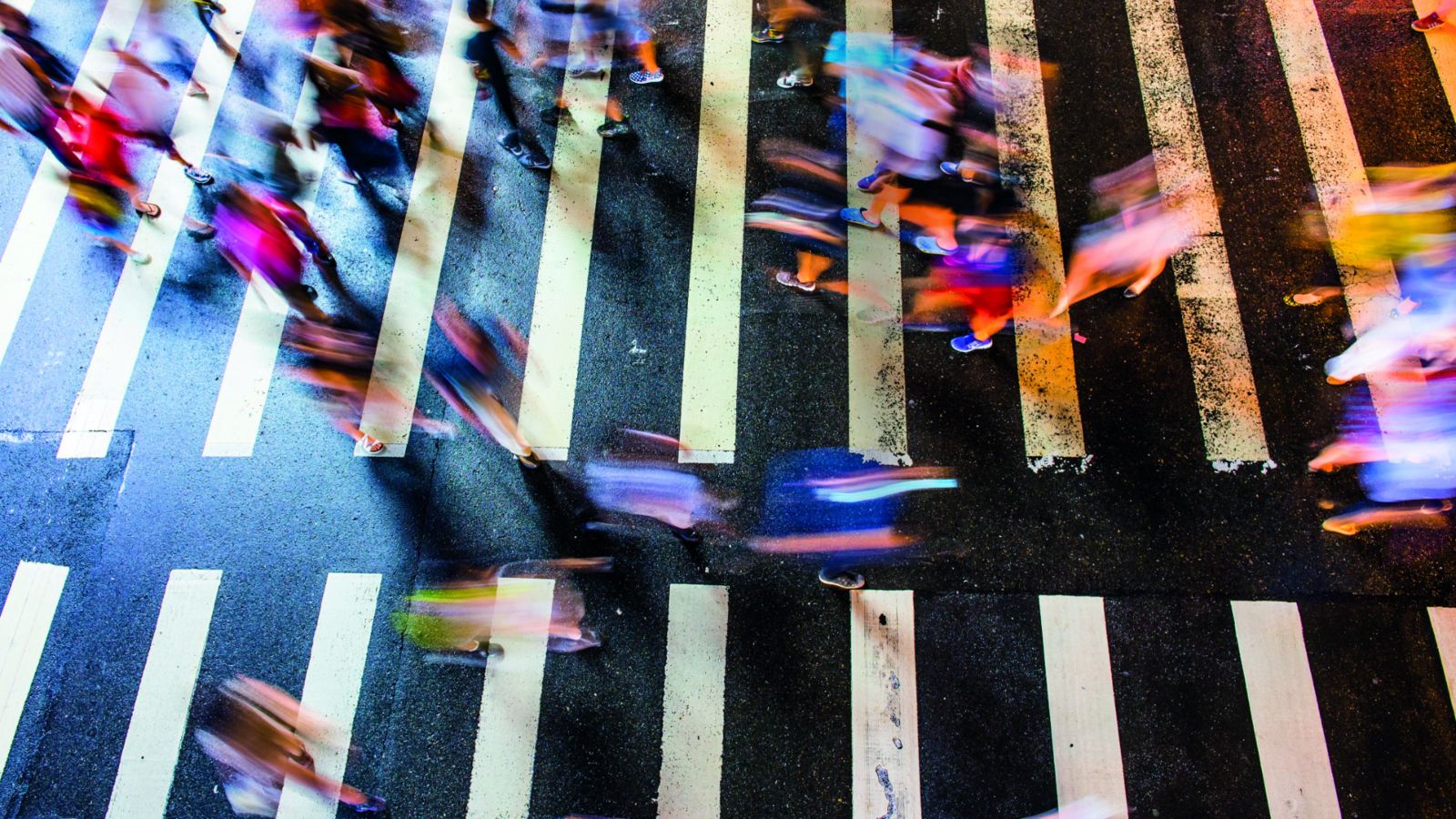 Birds eye view of several blurred people crossing both ways on a zebra crossing.