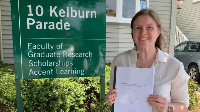 Lauren with a printed copy of her PhD thesis outside the Faculty of Graduate Research