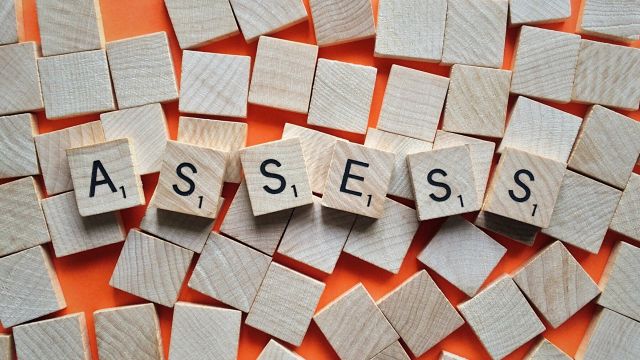 Wooden scrabble tiles spelling ASSESS
