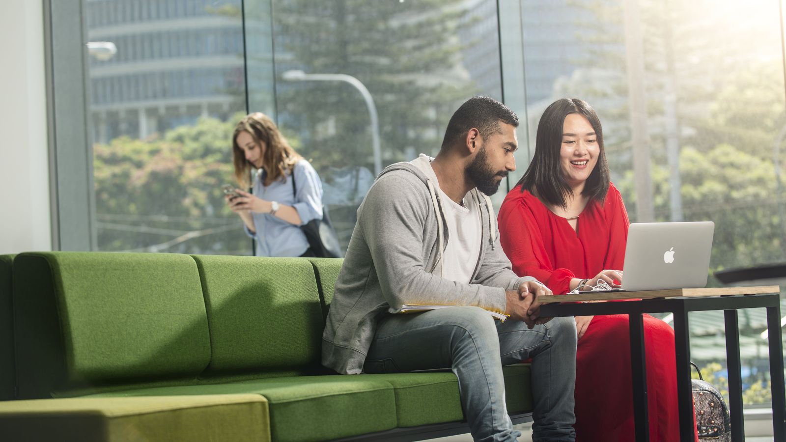 Two students look at laptop while sitting on a green couch at the University's Pipitea campus.