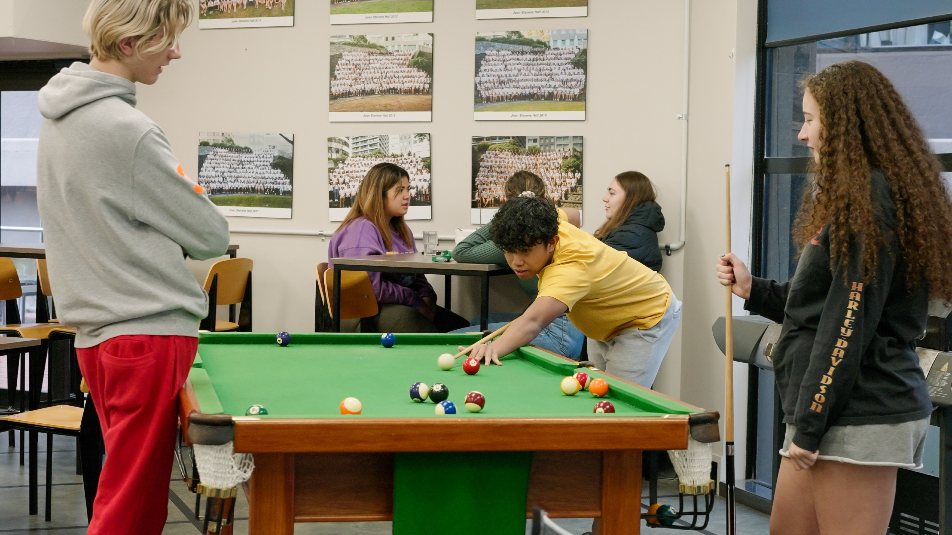 Three students playing pool in hall common room.