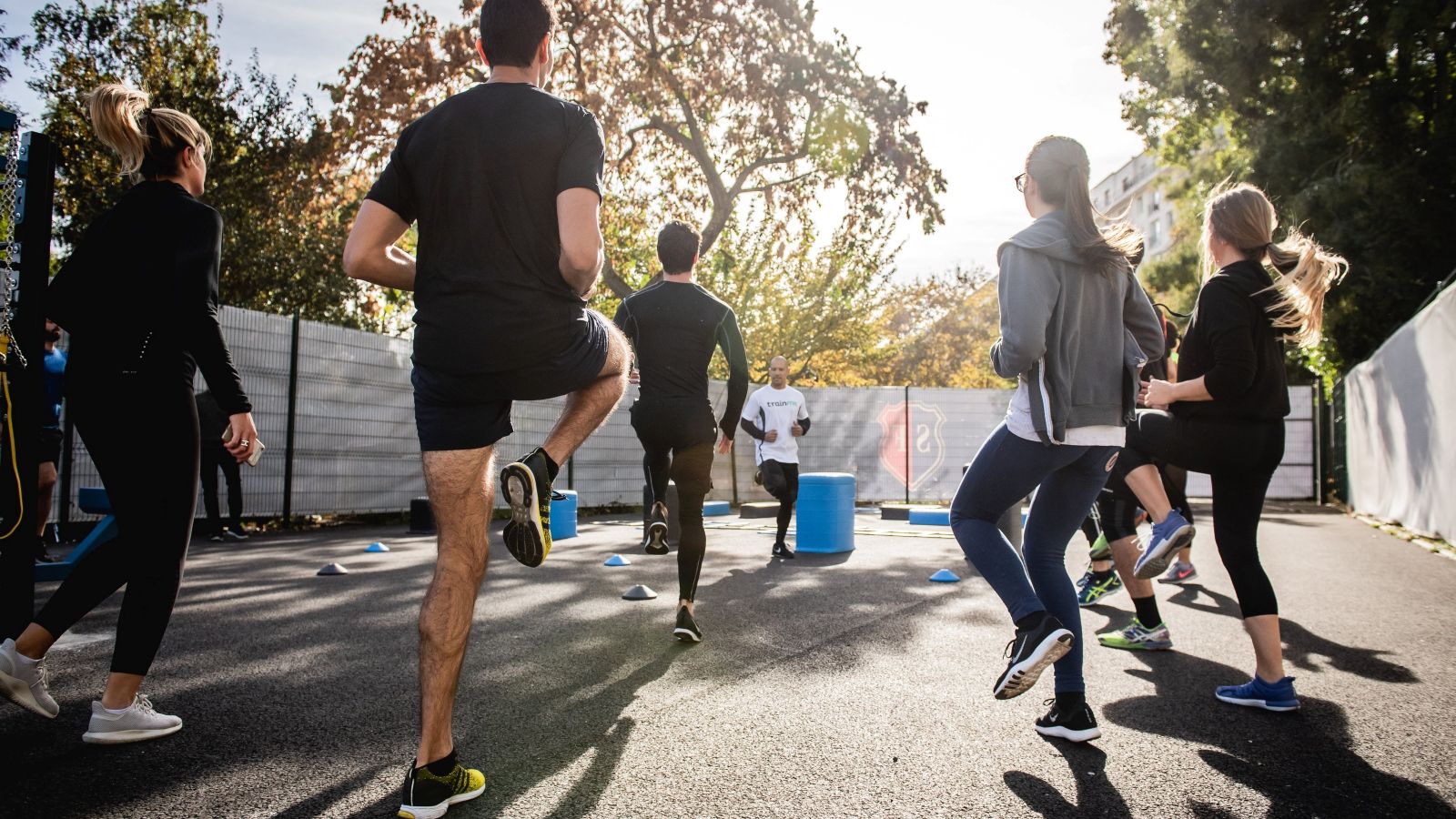 Group of people stand outdoors facing a fitness instructor.