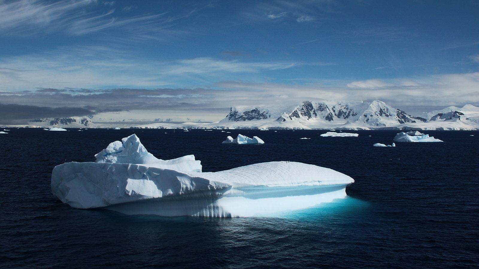 Iceberg in water with mountain range in the background.
