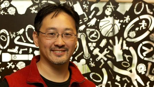 Computer programmer Milton Ngan in front of a printed backdrop.