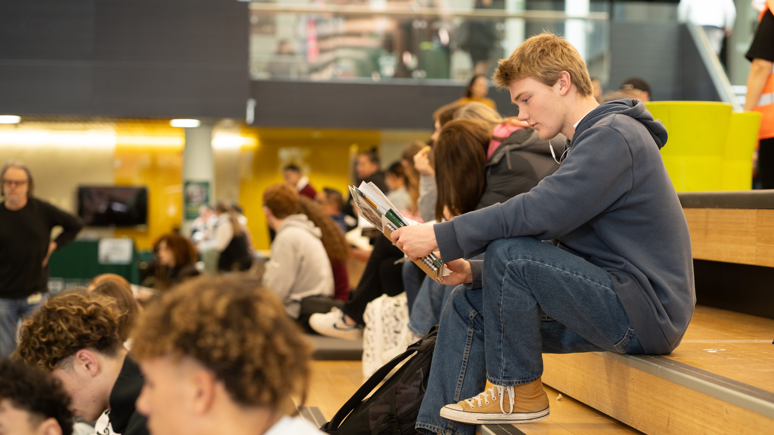 A prospective student sits on the steps in the Hub reading brochures.