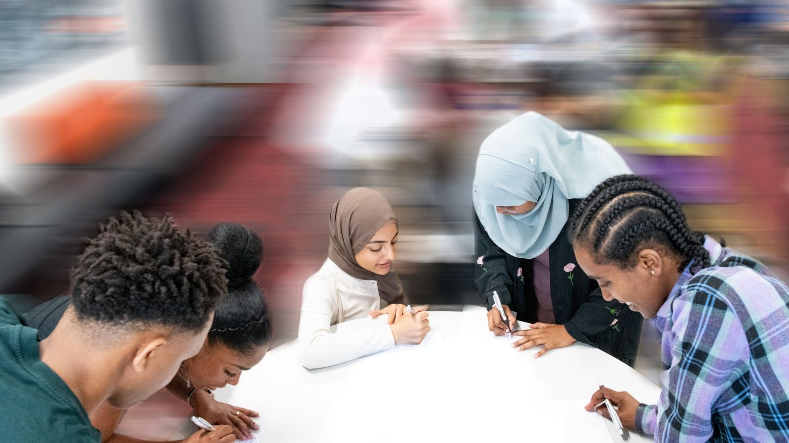 Five students writing together at a table in The Bubble with a blurred background.
