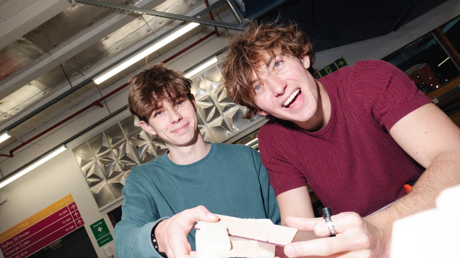 2 students smiling at the camera, holding a small wooden model