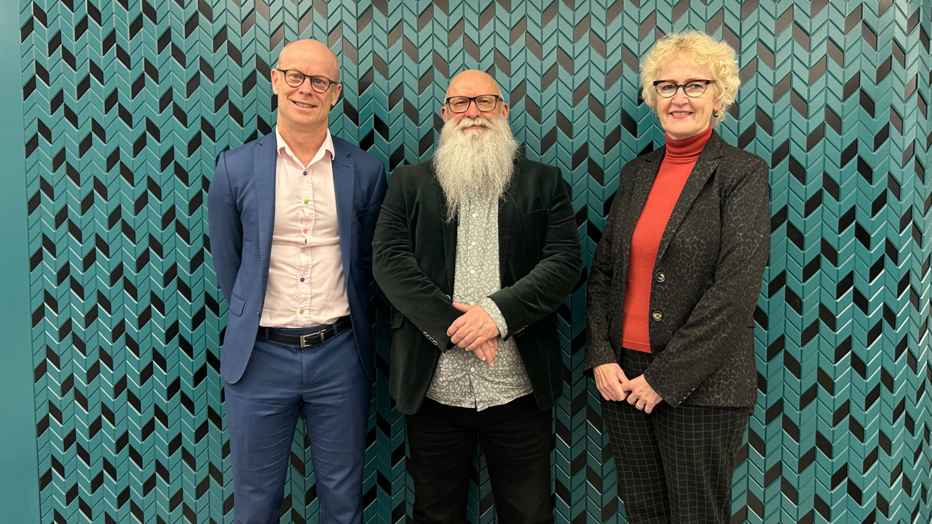 Three academics, two male, one female in front of a geometric teal green and black wall