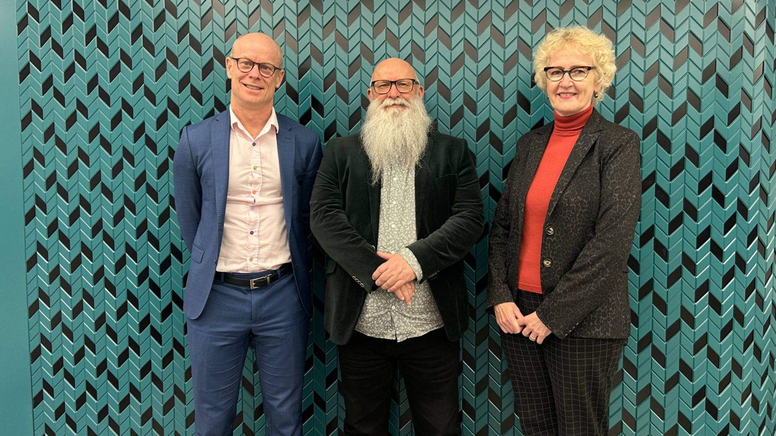 Three academics, two male, one female in front of a geometric teal green and black wall